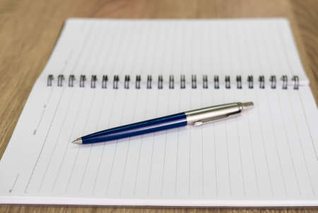 Closeup photo of ball pen on notebook on wooden deskの写真素材