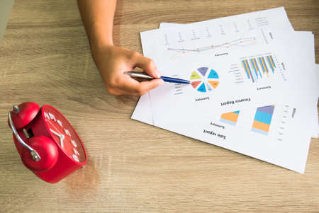 Closeup of male right hand holding pen points on colorful business graph in office top viewの写真素材