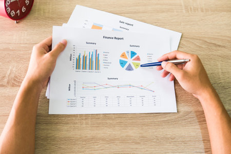 Closeup of male right hand holding pen points on colorful business graph in office top view