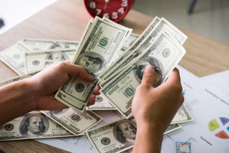 Closeup of Asian male hands counting bunch of dollars banknotes with business charts background for business, finance, tax and people conceptの写真素材