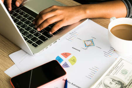 Asian female office worker typing on her laptop and working on business charts and mobile phoneの写真素材