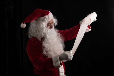 Santa Claus reading gift's list for children studio shot on black background for family, giving, season, Christmas, holiday, new year, travel, Christian and gathering conceptの写真素材