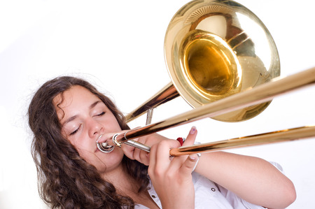 Teenage girl playing the trombone  Isolated on a white background  Studio shotの写真素材