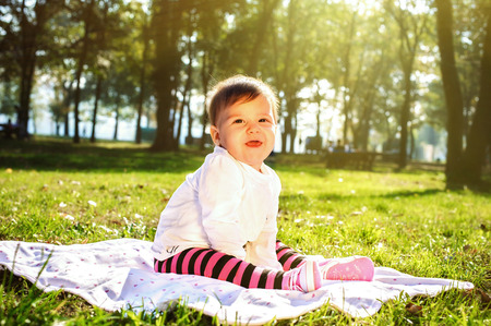 Cute smiling baby sitting on the sunny meadow in the forestの写真素材