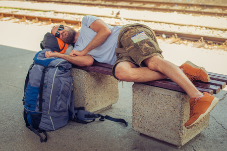 Handsome male backpacker tourist napping on a bench and baggage at the stationの写真素材