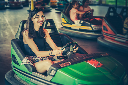 Cute young woman having fun in electric bumper car in amusement parkの写真素材