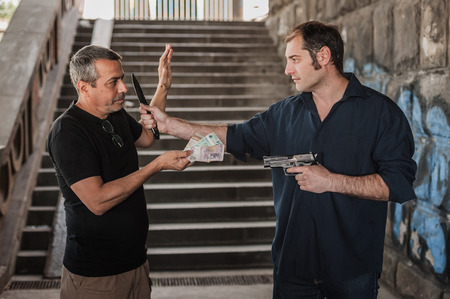 Robber with a gun and knife taking money from victim in a abandoned part of the cityの写真素材
