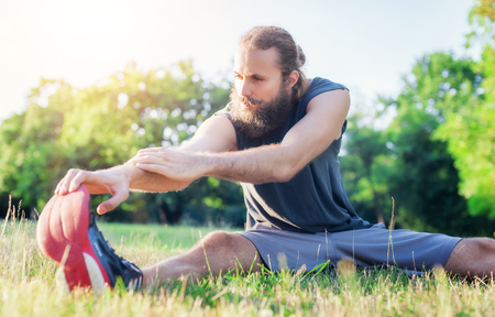Attractive fitness man stretching exercises outdoors on grassの写真素材