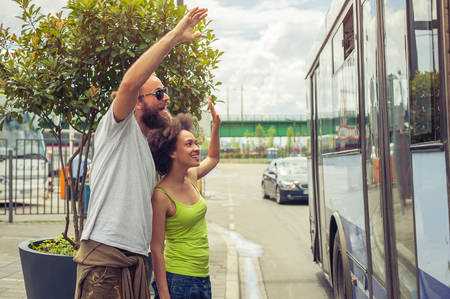 Young couple waving goodbye to their friends on the bus at bus stationの写真素材