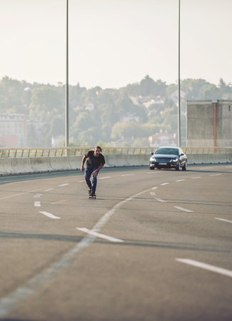 Professional skateboarder riding a skate over a city road bridge, through urban traffic. Free ride...