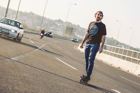 Professional skateboarder riding a skate over a city road bridge, through urban traffic. Free ride skateboardsの写真素材