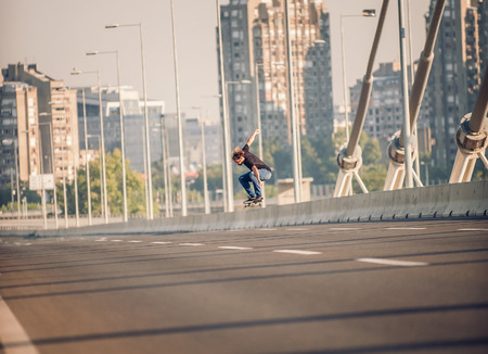 Skater doing tricks and jumping on the street highway bridge, through urban traffic. Free riding skateboardの写真素材