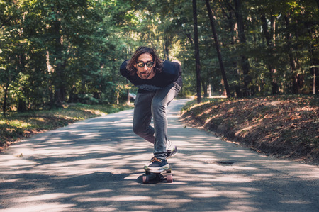 Skateboarder ride a longboard skateboard on the road through the forest. Freeride longboard skatingの写真素材