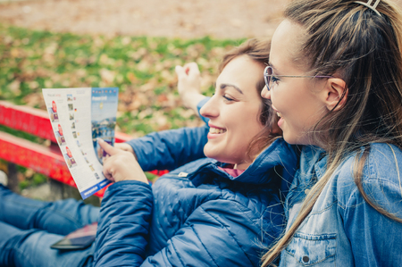Two women checking the city map, sitting on a benchの写真素材
