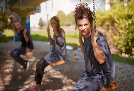 Three girl friends are swinging on the swings and enjoy the conversationの写真素材