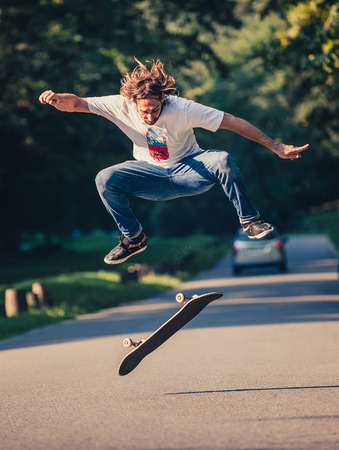 Action shot of a skateboarder skating, doing tricks and jumping on the road through the forest. Free riding skateboardの写真素材