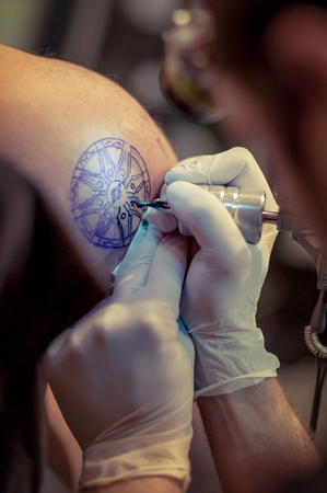 Master tattoo draws the blue paint on the clients tattooの写真素材