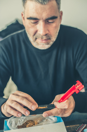 Smoker man roll domestic tobacco cigarettes using rolling machine. Close upの写真素材