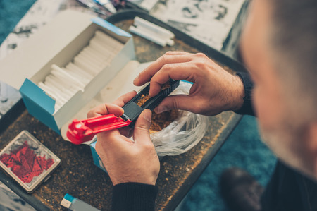 Smoker man roll domestic tobacco cigarettes using rolling machine. Close upの写真素材