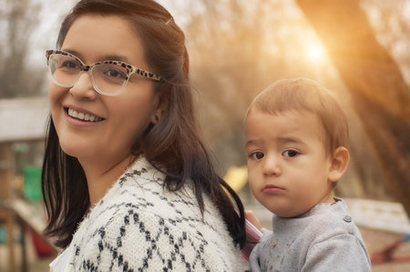 Portrait of a mother carrying her little baby in a baby carrier scarf in the park
