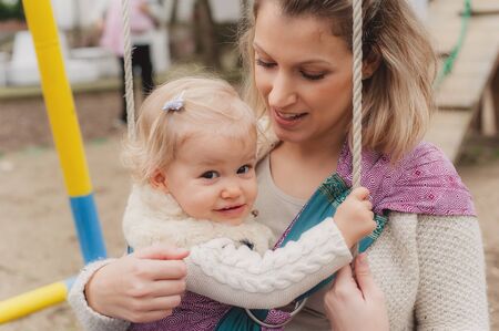 Closeup baby girl and his mother at swings in the parkの写真素材