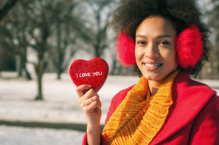 Smiling woman with ear warming and big red heart in winter day. Valentines Day