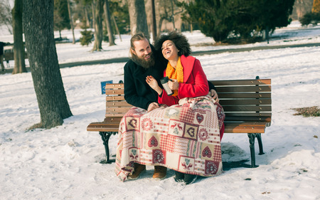 Loving couple with hot drinks sitting on bench in winter. Christmas timeの写真素材