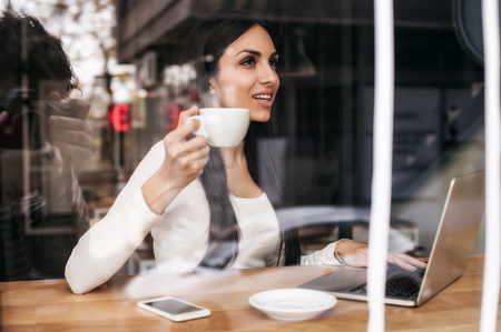 Portrait of smiling woman drinking coffee and surfing on internet. Cafe windowの写真素材