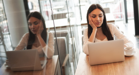 Portrait of smiling young woman drinking a coffee and surfing on internet on her laptop computerの写真素材