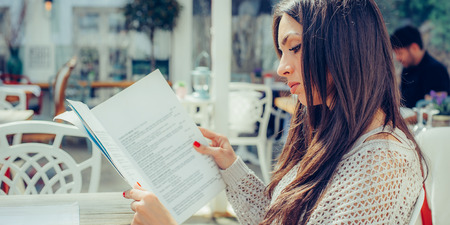 Beautiful woman looking at menu and ordering foods in restaurant. Close upの写真素材