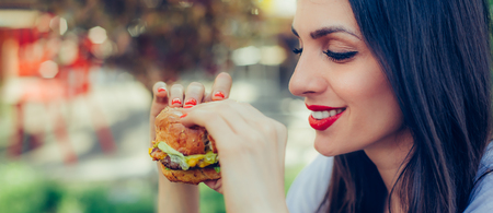 Portrait of a young happy woman eating tasty fast food burgerの写真素材