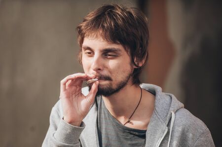 Closeup of young man smoke marihuana grass or hashish joint cigarette in abandoned ghetto part of the cityの写真素材