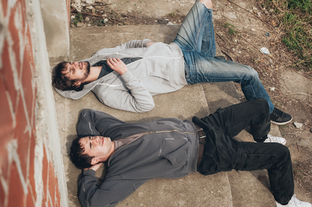 Two friends lying on the ground and smoke grass joint in abandoned ghetto part of the cityの写真素材