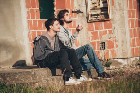 Two friends sitting on stairs and smoking cannabis or hashish joint in abandoned ghetto part of the cityの写真素材