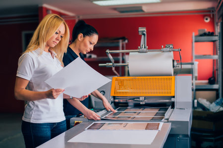 Two young woman working in printing factory. Printing Press