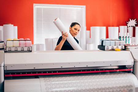 Young woman technician working on plotter and cutter machine in printing centar