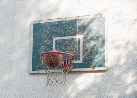 Ball basketball going through a small rustic old hoop with backboard on the wall in the shade of...