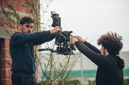 Behind the scene. Cameraman and assistant shooting the film scene with camera on outdoor locationの写真素材