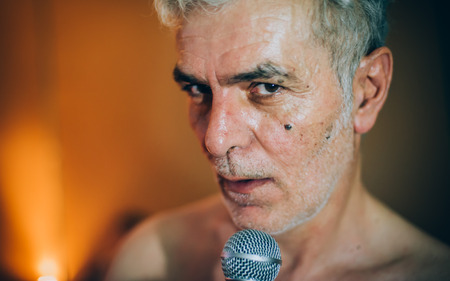 Behind the scene. Famous alternative male singer practice singing on the microphone in the messy recording music studio. Musician live singingの写真素材