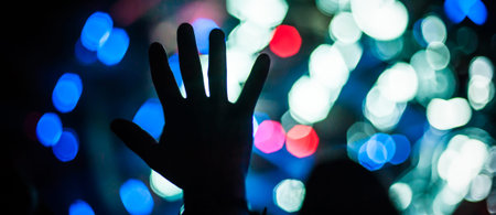 Silhouette of raised hands and arms in the air in front of the stage at a concert or a clubbing...