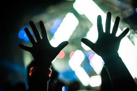 Silhouette of raised hands and arms in the air in front of the stage at a concert or a clubbing festival party of electronic musicの写真素材