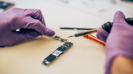 Technician repair microchip and motherboard of mobile phone in electronic smart phone technology service. Cellphone technology device maintenance engineerの写真素材