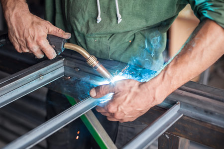 Industrial worker welding the steel structure in the workshop. Flies of spark from hot metal