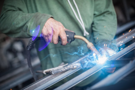 Industrial worker welding the steel structure in the workshop. Flies of spark from hot metal