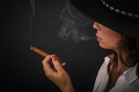 Portrait of sexy elegant lady woman with hat smoking cigar. Fashion glamour style. Studio shootの写真素材