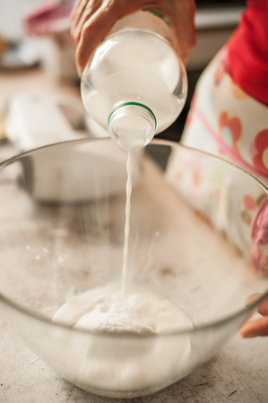 Woman pouring milk into glass bowl and making whipped cream. Close upの写真素材