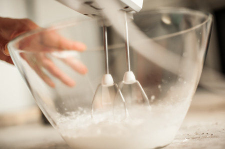 Woman holding mixer and making whipped cream in glass bowl. Close upの写真素材