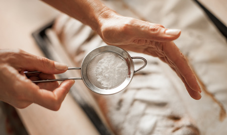 Female chef finishing sweet cake with sugar on the top. Close upの写真素材