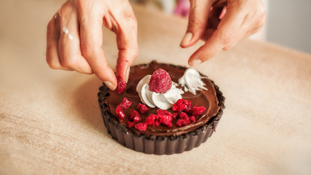 Woman chef preparing chocolate cake with whipped cream and raspberry. Close upの写真素材