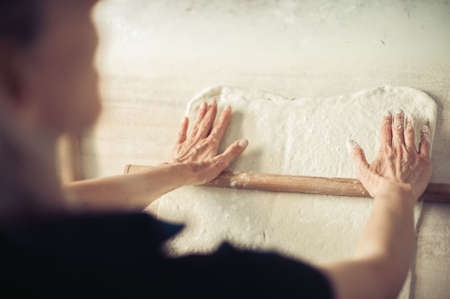 Woman rolling dough on wooden table with wooden rolling pin. Close upの写真素材